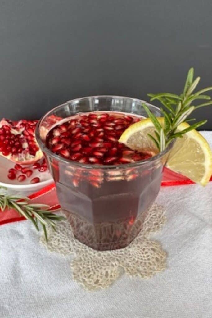 Pomegranate Fizz Mocktail garnished with rosemary, pomegranate seeds, and lemon slice in a festive glass